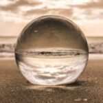 A glass sphere reflecting the sky and ocean on a sandy beach at sunset in Bonita Springs, FL.
