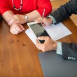 Business meeting at a wooden table with consultant reviewing documents and using a digital tablet.