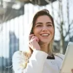 Confident businesswoman using her tablet and phone, smiling outdoors in sunlight.